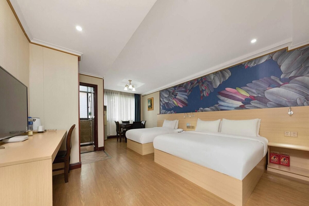 A hotel room with a bed, desk, and a painting on the wall.