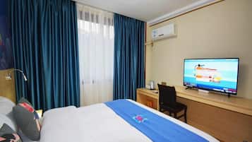 A hotel room with a bed, a desk, a television, and a window with curtains.