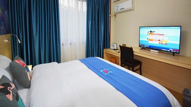 Habitació d'hotel amb llit, escriptori, televisió i finestra amb cortines.