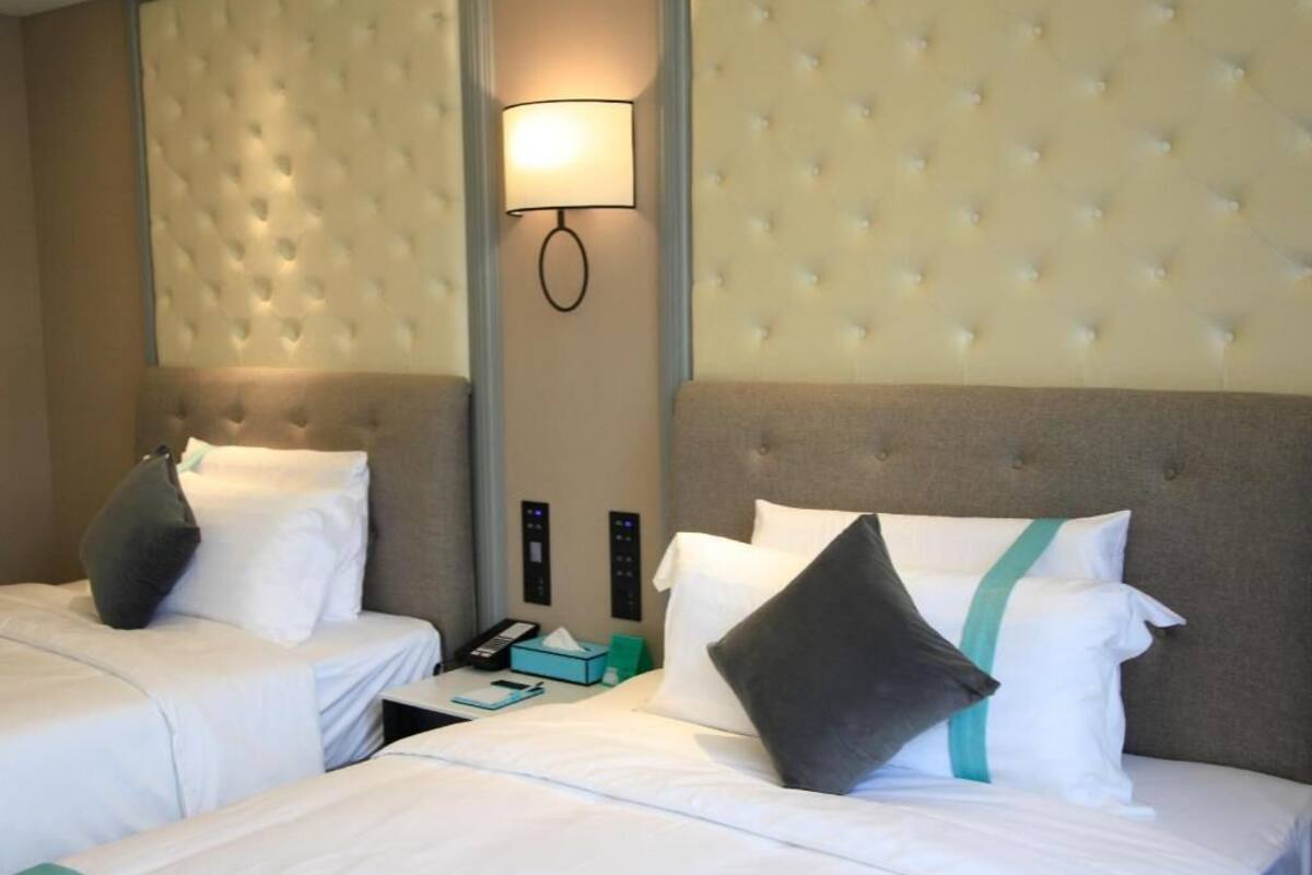 Une chambre d’hôtel avec deux lits, une lampe fixée au mur, un panneau de commande et une table de chevet avec un téléphone et des mouchoirs.