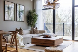 A modern living room with a sofa, coffee table, and a large window with a view of trees. - Modern forest villa with sea views and sauna (Trollhättan)