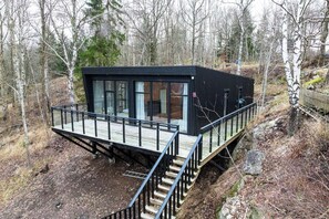 A modern cabin with a deck, large windows, and a staircase leading to the entrance. - Modern forest villa with sea views and sauna (Trollhättan)