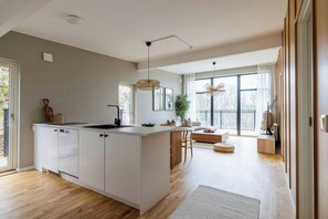 A modern kitchen with a large island, a dining area with a wooden table and chairs, and a large window providing natural light. - Modern forest villa with sea views and sauna (Trollhättan)