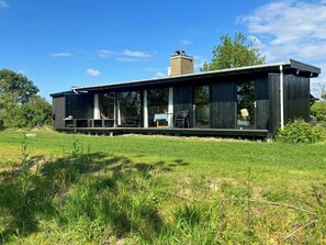 Ein modernes Haus mit einer großen Terrasse, einem Schornstein und einem Rasenstück.