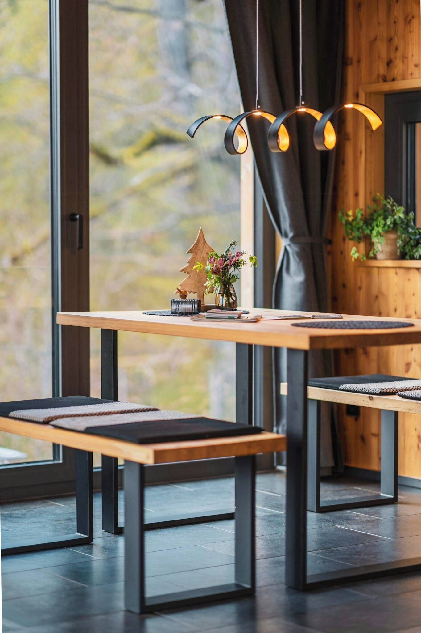 A modern dining area with a wooden table, black metal chairs, and a unique pendant light.