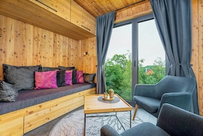 Ein Holzinnenraum mit einer Couch, einem Tisch und Blick durch ein großes Fenster.