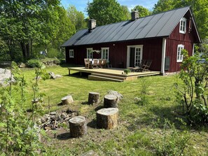 Une maison en bois rouge avec une terrasse, entourée d’une cour verdoyante et d’arbres.