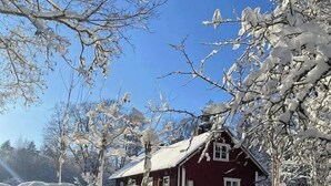 Una casa rossa con un muro di pietra davanti, circondata da alberi innevati.