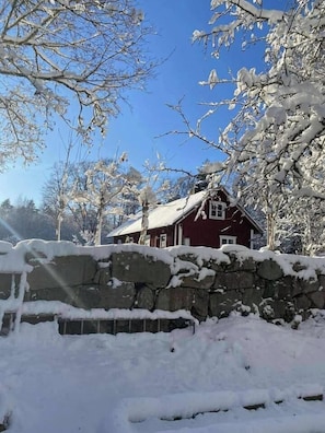 Ein rotes Haus mit einer Steinsäule im Vordergrund, umgeben von schneebedeckten Bäumen.