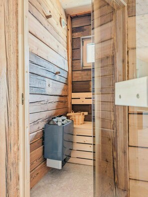 Ein Holzinnenraum mit Sauna, Mülleimer und einer hölzernen Sitzbank.