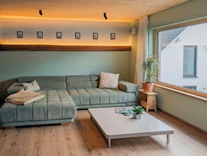 Ein modernes Wohnzimmer mit Ecksofa, Couchtisch und einer Pflanze vor einem Fenster.