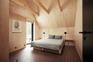 Ein Schlafzimmer mit schrägem Holzboden, einem Bett mit gestreifter Bettdecke und einem gerahmten Kunstwerk an der Wand.