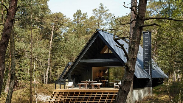 Eine Hütte mit einer Holzdielen-Terrasse, einem Essbereich und einem großen Fenster.