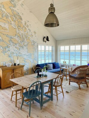 A room with a wooden table, chairs, a map on the wall, and a view of the sea through large windows. - Island house on private island with sea view (Östhammar)