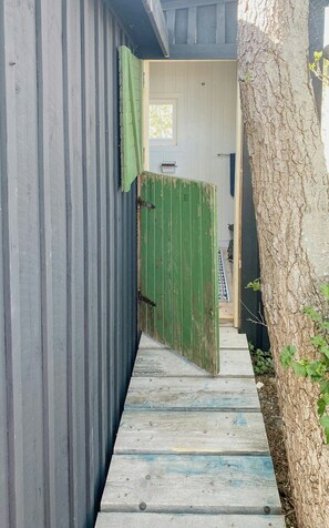 A narrow wooden pathway leading to a door with a green gate, flanked by a wooden wall and a tree. - Island house on private island with sea view (Östhammar)
