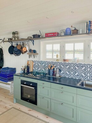 A kitchen with a stove, oven, and hanging utensils. - Island house on private island with sea view (Östhammar)