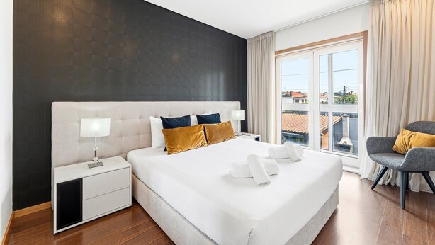 Een moderne hotelkamer met een groot bed, een nachtkastje, een stoel en uitzicht op de stad door het raam.