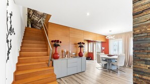 Een modern interieur met een houten trap, een eethoek met tafel en stoelen, en een keuken met kasten en een vaas met bloemen.