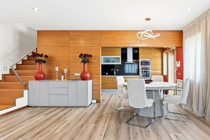 Eine moderne Küche mit Holzausstattung, ein Essbereich mit weißem Tisch und Stühlen sowie eine Treppe mit einer roten Vase auf der Zwischenebene.
