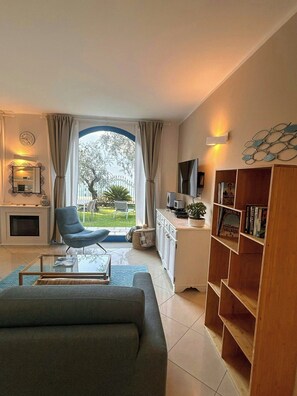 A modern living room with a sofa, a coffee table, a TV, a bookshelf, and a view of the outdoors. - Lakefront house with garden on Monte Isola (Monte Isola)