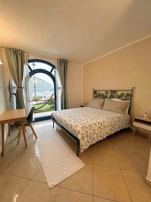A bedroom with a bed, a desk, a chair, a nightstand, and a view of a mountain through a window. - Lakefront house with garden on Monte Isola (Monte Isola)
