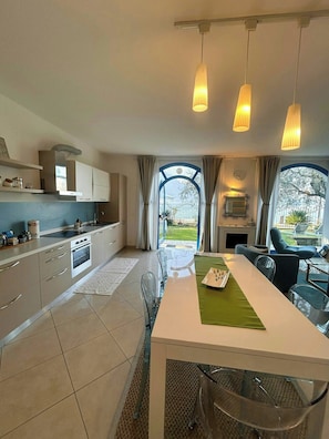 A modern kitchen with a dining area, large windows, and hanging pendant lights. - Lakefront house with garden on Monte Isola (Monte Isola)