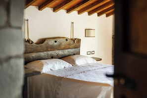 A rustic wooden bed with a headboard, two pillows, and a bedside table with a mirror. - Historic apartment in Tuscan village (Londa)