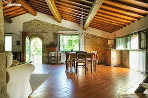 A spacious room with a wooden ceiling, stone walls, a tiled floor, a dining table with chairs, and a fireplace. - Historic apartment in Tuscan village (Londa)