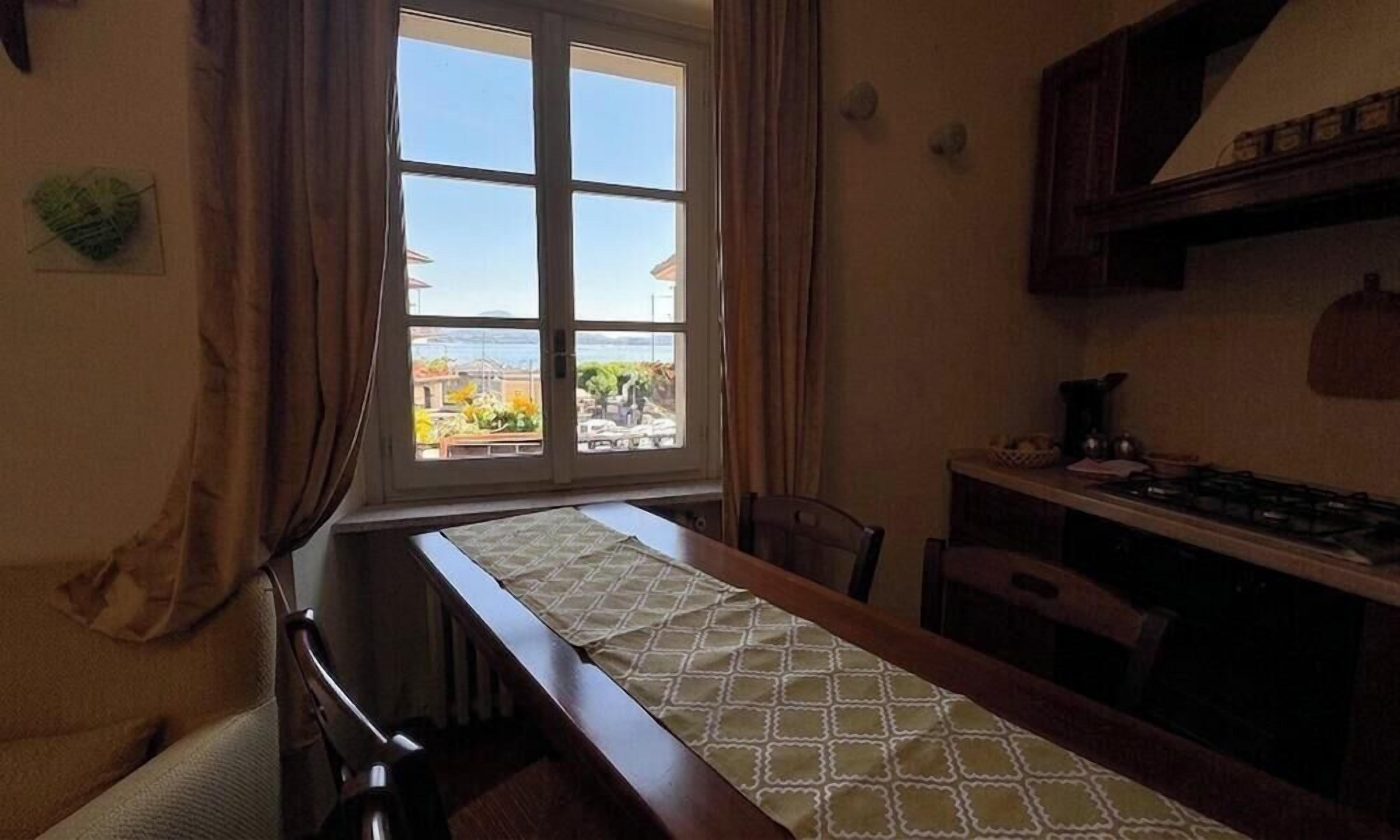 Un comedor con una mesa, sillas, un ventanal con cortinas y una zona de cocina con estufa.