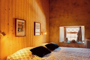 A wooden-paneled room with a bed, a framed poster, a window with a view, and a radiator.