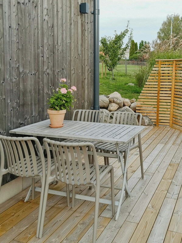 An outdoor patio with a wooden table and chairs, a potted plant, and a view of a garden with rocks and a wooden fence. - Modern guest house near the sea in Brösarp (Brösarp)