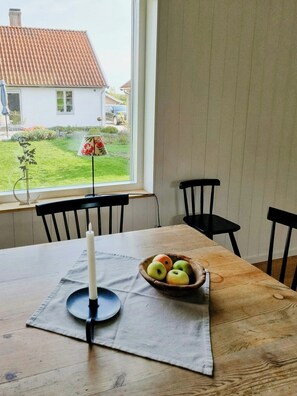 Ein Esstisch mit Kerze, Obstschale und Blick auf ein Haus durch ein Fenster.