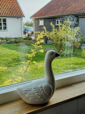 Eine weiße Keramik-Ente auf einem Fensterbrett mit Blick auf ein Haus und einen Garten.