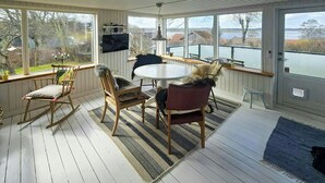 A sunroom with a round table, chairs, a TV, and a view of a lake. - Cozy cottage with fjord view in Hjarbæk (Løgstrup)