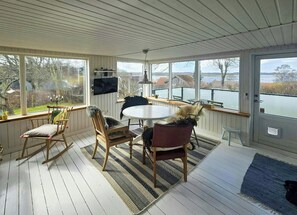 A sunroom with a round table, chairs, a TV, and a view of a lake. - Cozy cottage with fjord view in Hjarbæk (Løgstrup)