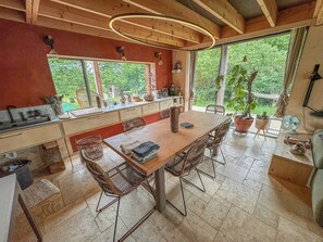 Une cuisine avec une table en bois, des chaises en osier et de grandes fenêtres.