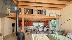 A spacious interior with a high ceiling, a kitchen area, a dining space, and a seating area with a sofa and ottoman. - Natural materials house near Nancy (Dommartemont)