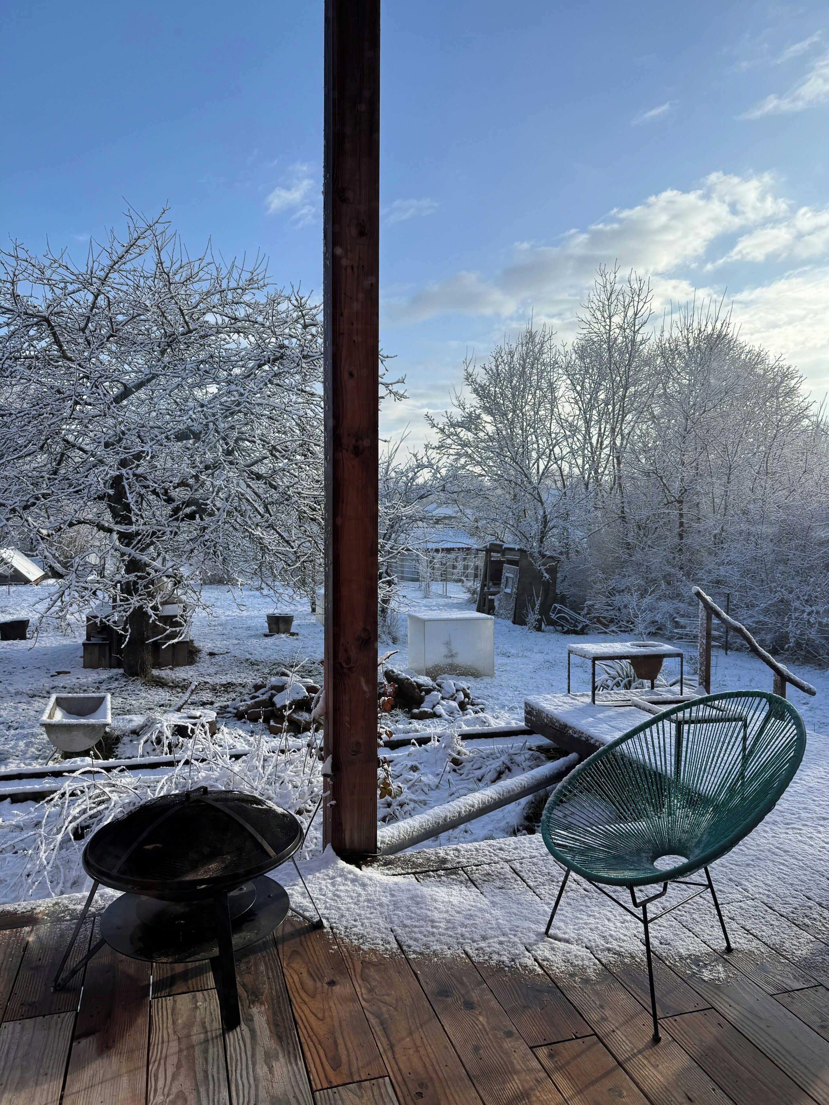 Una terraza de madera con una parrilla, una silla verde y árboles cubiertos de nieve.