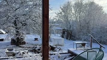 Una terraza de madera con una parrilla, una silla verde y árboles cubiertos de nieve.