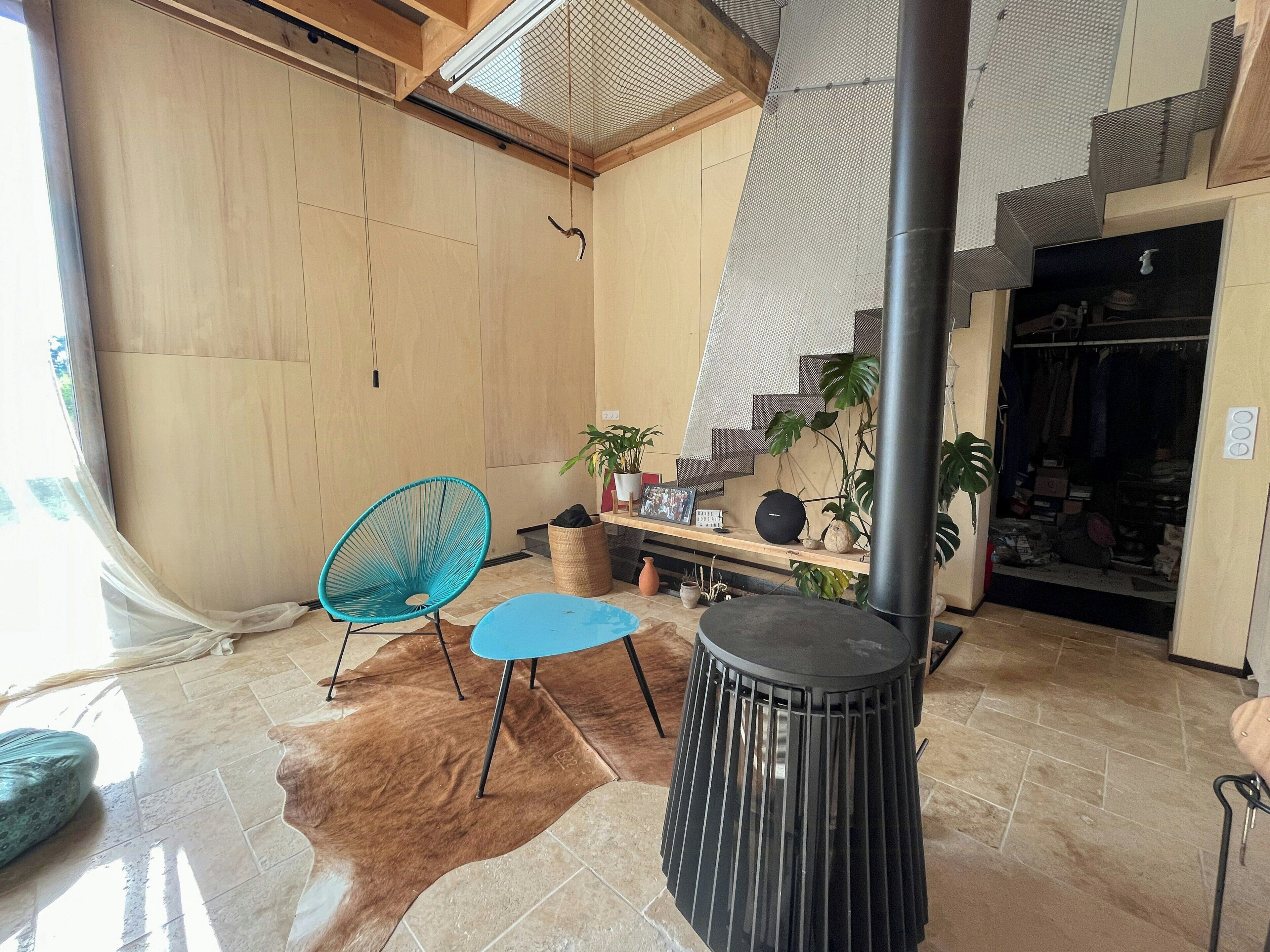 A room with a wooden wall, a black heater, a blue chair, a cowhide rug, and a shelf with plants and a picture frame.