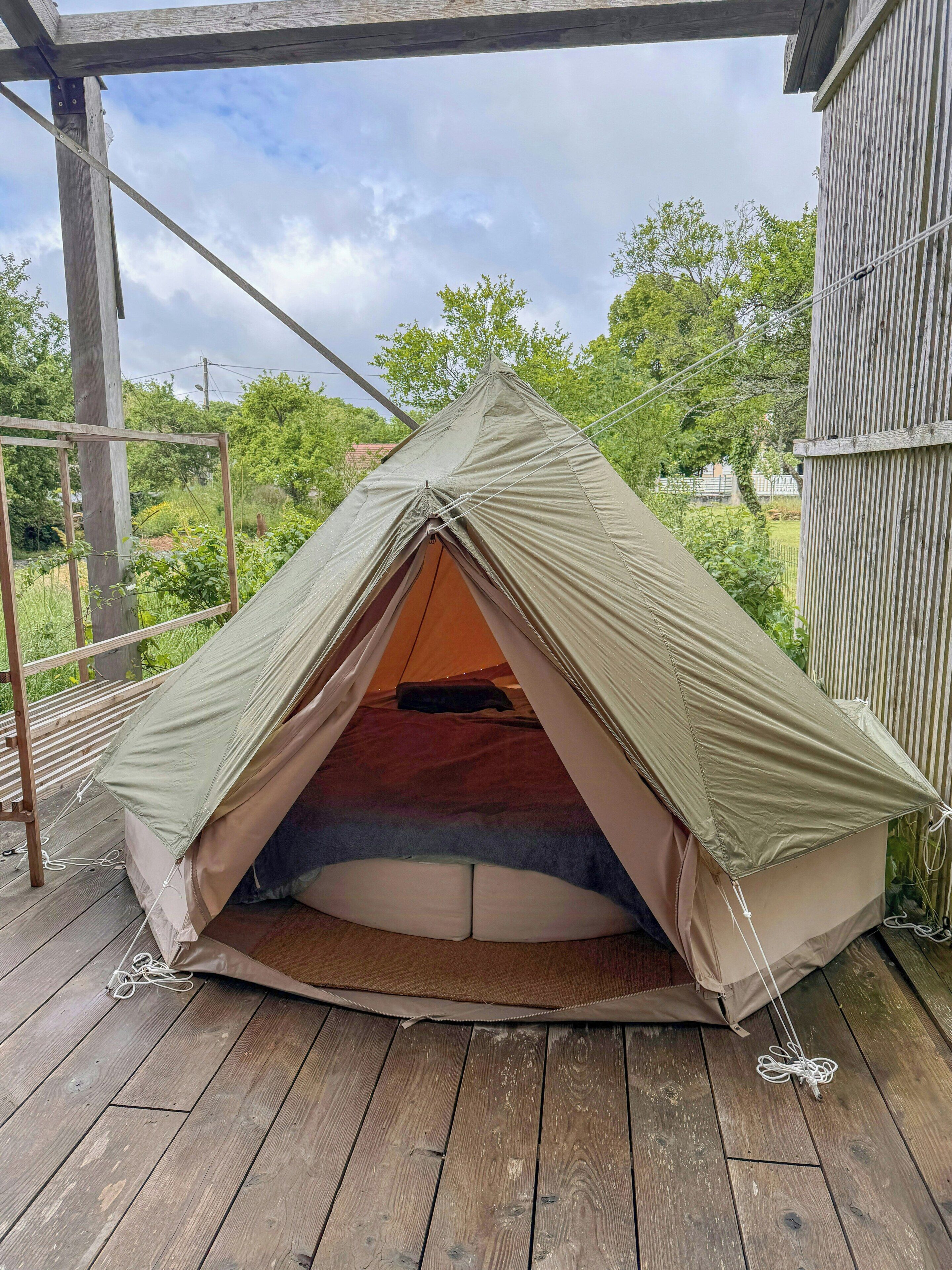 Une tente installée sur une terrasse en bois, avec vue sur les arbres et un bâtiment en arrière-plan.
