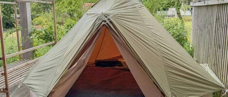 A tent on a wooden deck with a view of trees and a building in the background.
