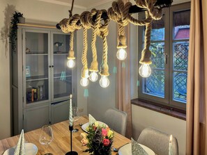 A dining area with a wooden table, chairs, a candle, a vase with flowers, and a bookshelf. - Thatched-roof house at Stettiner Haff (Kamminke)
