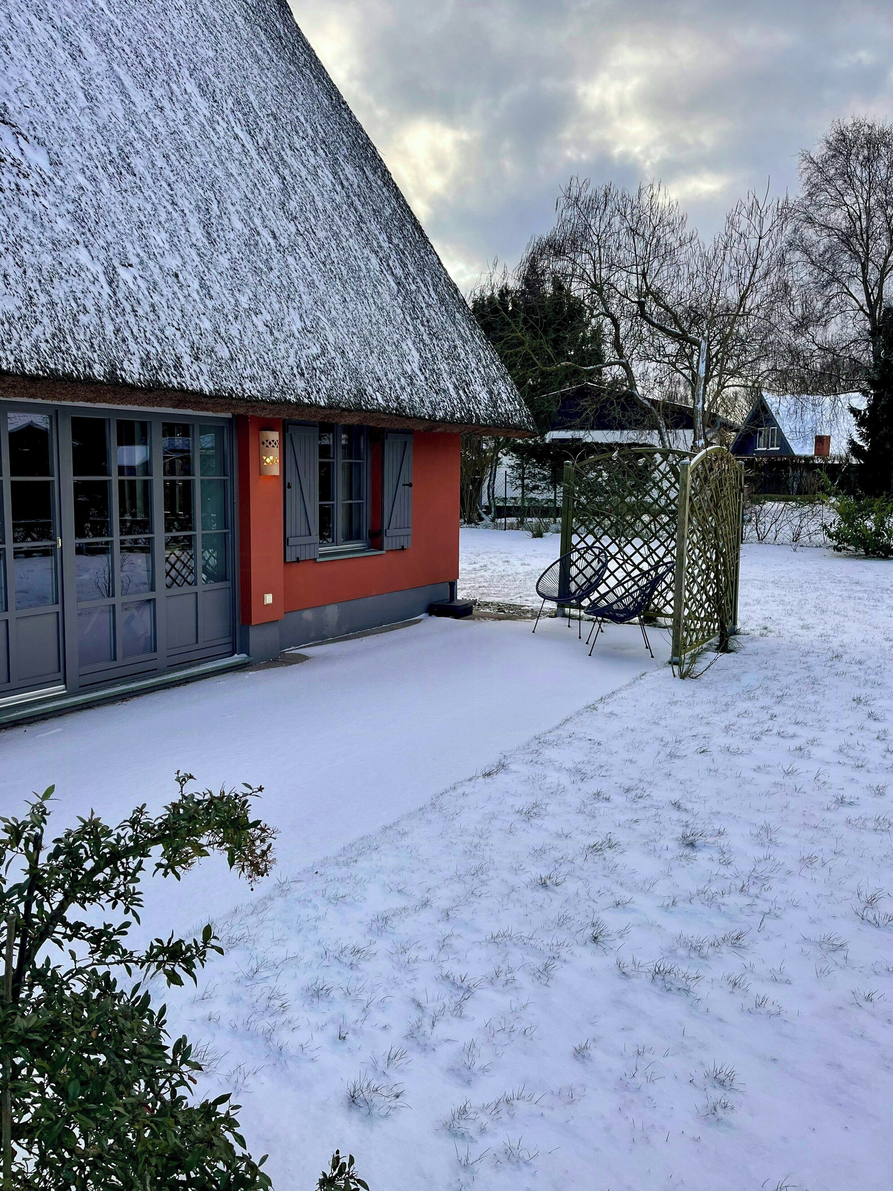 Una casa con techo de paja, pared exterior roja y un patio cubierto de nieve.