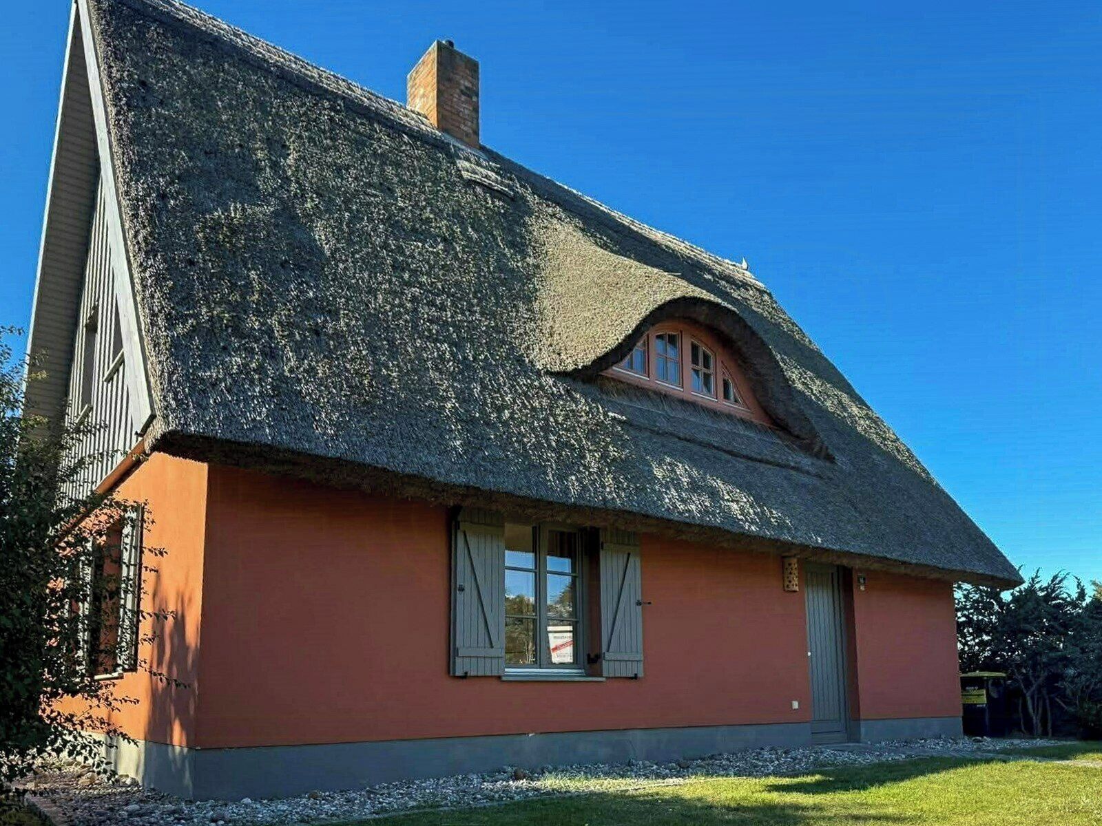 Ein Haus mit einem Strohdach, einem kleinen Fenster mit Fensterläden und einem Schornstein.