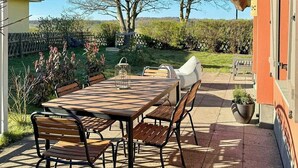 Un patio con mesa y sillas, techo de paja y vista a árboles y una valla.