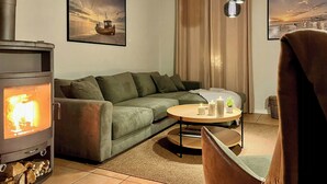 Una sala de estar con estufa de leña, un sofá, una mesa redonda de centro y dos cuadros enmarcados en la pared.