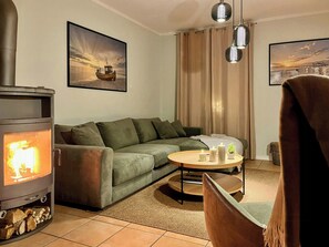 En stue med brændeovn, sofa, rundt sofabord og to billeder i rammer på væggen.