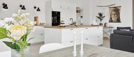 Una cocina moderna con armarios blancos, encimera de madera y una zona de comedor con mesa y sillas.