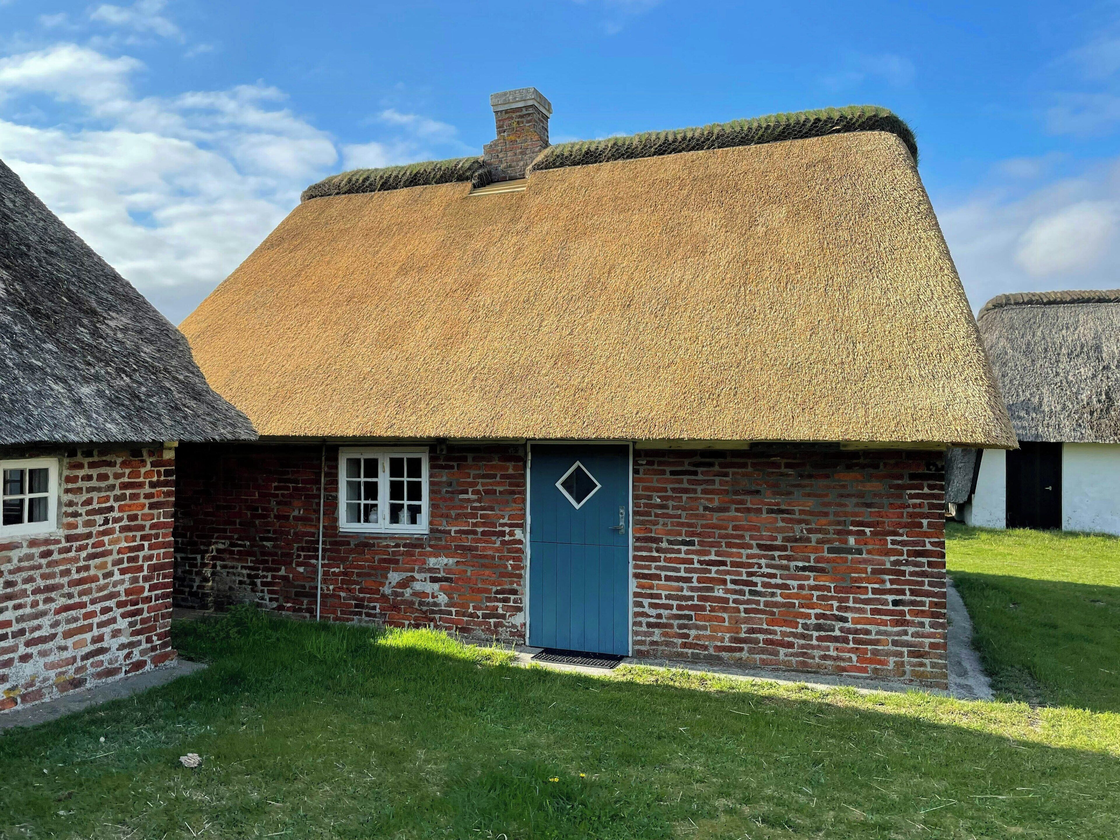 Een traditioneel huis met rieten dak, een bakstenen gevel, een blauwe deur en een klein raam.